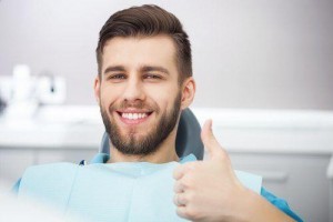 Bearded young man sitting in dental chair giving a thumbs up with a smile.