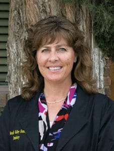 Profile shot of Teri Tingen. Dressed in navy blue lab coat, floral shirt, medium brown hair, and smiling.