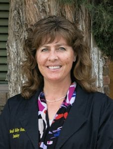 Profile shot of Teri Tingen. Dressed in navy blue lab coat, floral shirt, medium brown hair, and smiling.