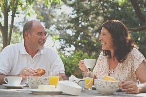 A middle aged man and woman laughing and talking while having a tea party