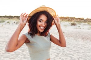 A young girl holding her hat while wearing it and smiling