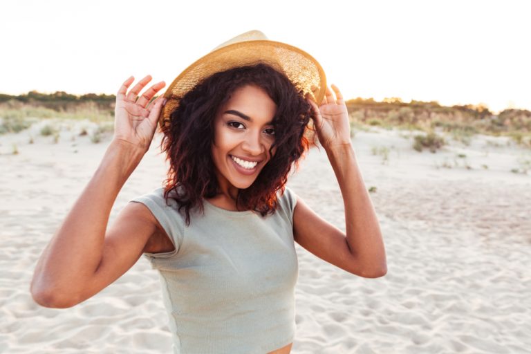 A young girl holding her hat while wearing it and smiling