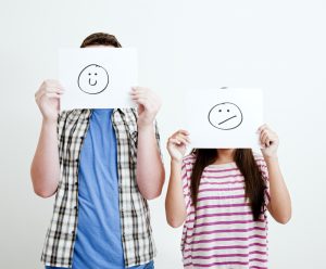 Two children holding papers with faces drawn on them