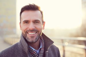 A smiling middle aged man with the sun shining behind him