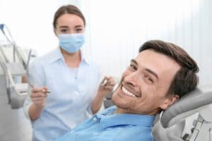 A patient in a dental chair smiling with dental assistant next to him