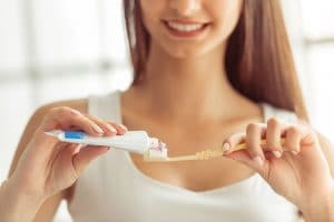 A woman smiling while putting toothpaste on a toothbrush