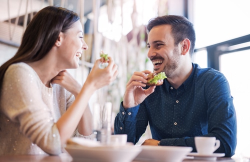A couple smiling and laughing and eating food on a date